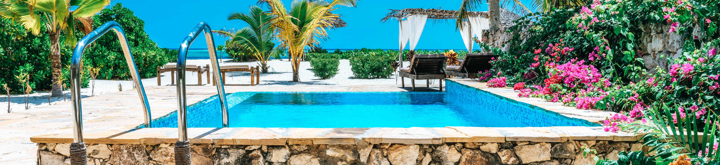 Pool mit Liegewiesen, Palmen und blühenden Büschen